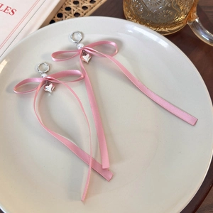 Dettaglio di orecchini a fiocco rosa con ciondolo a cuore e perla su un piatto bianco