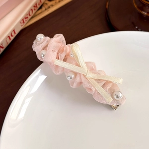 Détail d'une pince à cheveux en dentelle rose avec perles blanches et nœud en ruban crème
