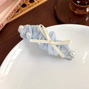 Détail d'une pince à cheveux en dentelle bleue avec perles et nœud sur une assiette