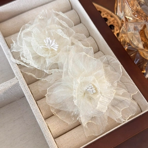 Detailed close-up of white organza floral earrings with pearl bead center on linen base