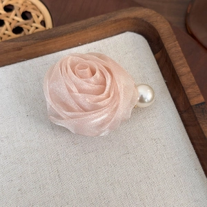 Détail de la pince à cheveux rose en organza avec perle sur plateau en bois et lin