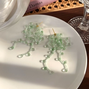 Gros plan de boucles d'oreilles en perles vert menthe avec pompons sur une assiette blanche