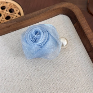 Vue macro d'une pince à cheveux rose en tulle bleu clair avec perle sur plateau bois