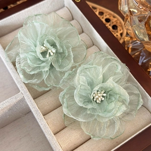 Close-up of light green organza flower earrings with delicate beads on a rustic linen lining
