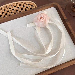 Gros plan d'une rose en tulle rose avec de longs rubans crème sur un plateau en bois