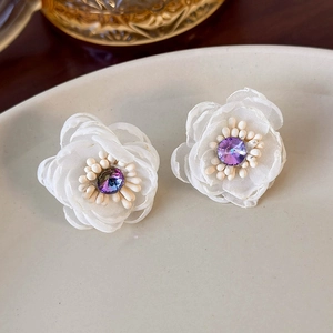 Detailed close-up of white mesh flower earrings with purple crystal and pearl center