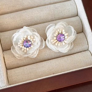 Detailed macro view of delicate white mesh flower earrings with purple crystal centers