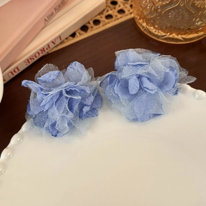 Close-up of blue fabric flower earrings on a white wavy ceramic plate in a French setting