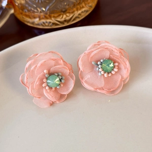 Detail of pink mesh fabric flower earrings with crystal center on a ceramic plate