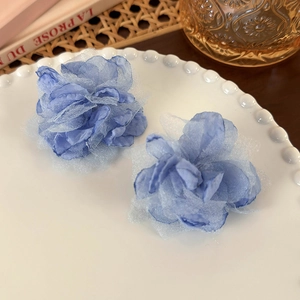 Detailed close-up of blue fabric flower earrings with mesh layers on a ceramic plate