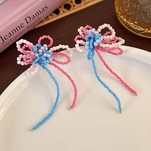 Detail of handmade beaded flower earrings with colorful tassels on a white ceramic plate