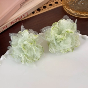 Detailed macro view of light green organza flower hair clips on a decorative white ceramic plate