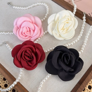 Detailed macro of satin camellia flower fabric brooch with lustrous pearl necklace accent