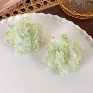 Close-up of light green mesh fabric flower earrings on a white porcelain dish