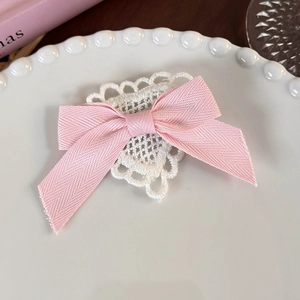 Detail of pink ribbon bow hair clip with white heart crochet lace on ceramic plate