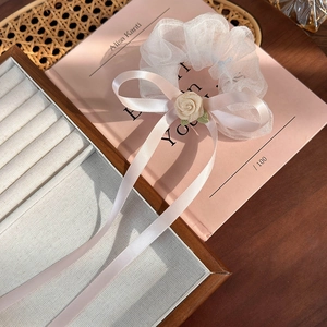 Détail d'un chouchou en maille blanche avec un nœud en satin rose et une rose en tissu