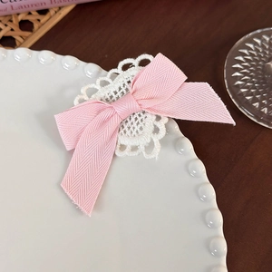 Detail view of pink bow hair clip with white lace trim on a decorative pearl plate