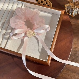 Détail d'un chouchou en organza rose avec un ruban blanc et une petite rose en tissu