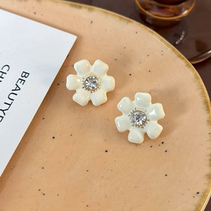 Gros plan détaillé des boucles d'oreilles fleurs en émail crème avec un strass central