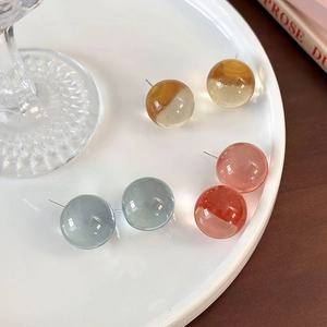 Translucent resin ball stud earrings in amber blue and coral colors on a white plate