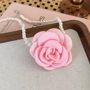Close-up of pink fabric camellia flower and white pearl necklace on a vintage display tray