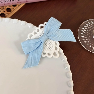 Detail of light blue bow hair clip with white lace trim on an elegant ceramic plate