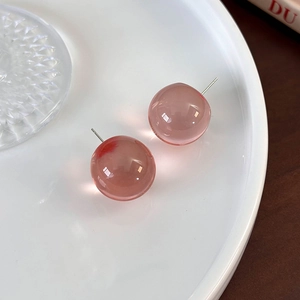 Detail of pink resin ball earrings with transparent finish on a ceramic tray