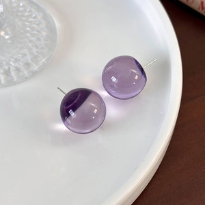 Macro detail of transparent purple resin ball earrings on a white ceramic tray