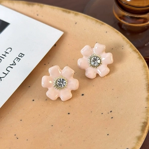 Détail macro de boucles d'oreilles fleurs roses avec cristal brillant sur plateau beige