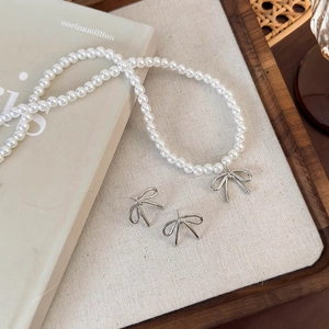 Elegant pearl necklace set with silver bow pendant and matching stud earrings on a wooden tray