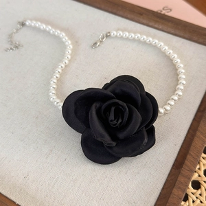 Detail of elegant black satin camellia flower with white pearl necklace and silver clasp