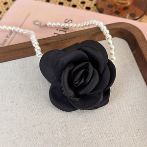 Close-up of a large black satin camellia flower on a vintage pearl necklace