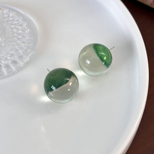 Detailed close-up of spherical resin stud earrings with green swirl design on a ceramic tray