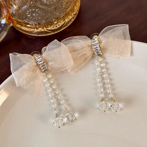 Close-up of champagne mesh bow earrings with long tassels and crystal beads on a tray