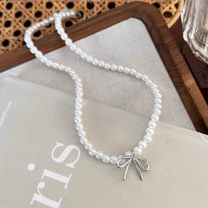 Detail shot of the elegant pearl necklace with silver bow pendant on art books