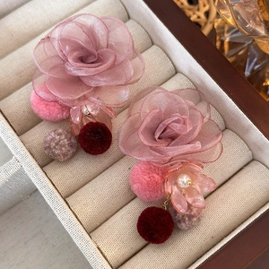 Detail of pink mesh flower earrings with plush pom poms and pearl accents on a tray