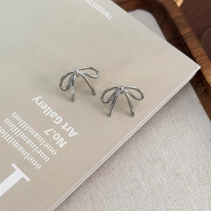 Detailed view of silver bow-shaped stud earrings placed on a wooden tray with a magazine