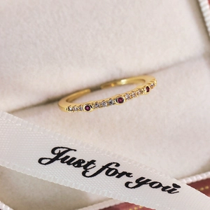 Gros plan d'une bague dorée sertie de zircons rouges dans son coffret cadeau beige