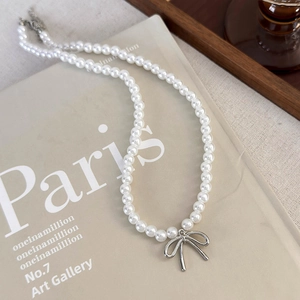 Detailed view of elegant pearl necklace with silver bow pendant on a French magazine background
