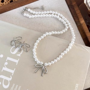 Detail view of pearl necklace and bow earrings set on elegant beige fabric backdrop