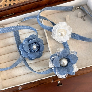 Detailed macro shot of denim lace flower chokers with elegant pearl centers in wood box