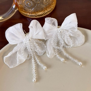 Detailed view of white mesh bow earrings with crystal tassel and faux pearl accents