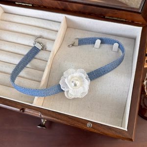 Detail of blue denim choker with white lace flower and pearl in elegant jewelry box