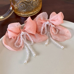 Close-up of pink silk bow hair clips with bead tassels and pearls on a ceramic dish