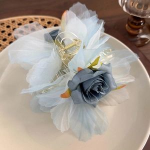 Dettaglio molletta per capelli a fiore in organza azzurra con rosa su piatto bianco