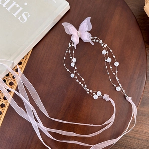 Detail of pink butterfly hair chain with pearls and ribbons on a vintage wooden tray