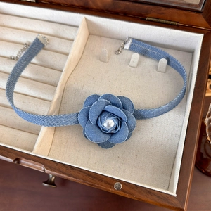 Detail of blue denim flower choker featuring a polished pearl center on rustic wood