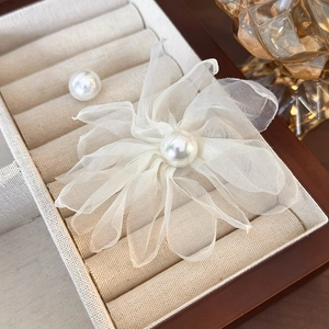 Close-up of white organza flower earrings with a pearl center on a beige velvet tray