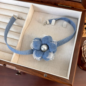 Detail of denim flower choker with white lace edges and pearl center in a jewelry box