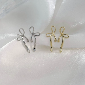 Minimalist bow ribbon stud earrings in gold and silver finish on silk fabric background